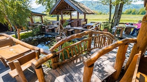 Eine Holzterrasse mit rustikalen Möbeln, ein kleiner Teich und ein Pavillon mit Strohdach.