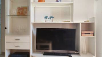 Un meuble de rangement blanc pour appareils multimédias, avec un téléviseur à écran plat, des étagères ornées d’objets décoratifs et une petite table sur laquelle repose une télécommande.