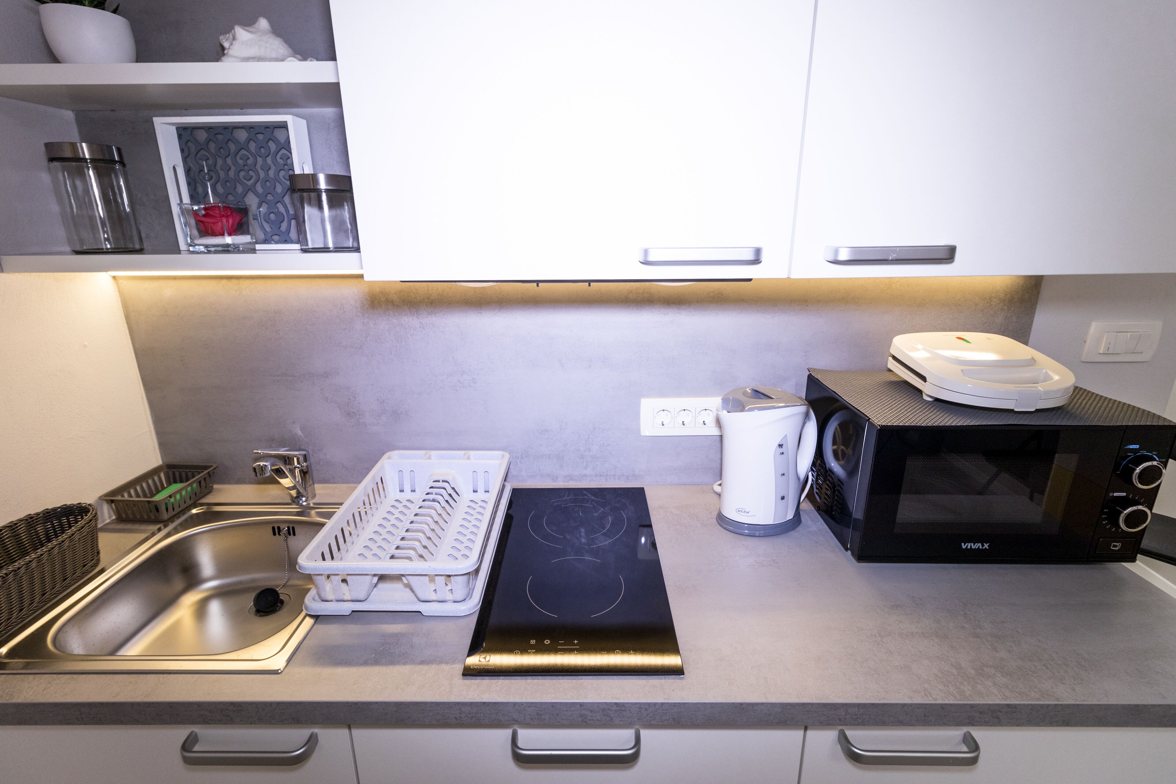 A kitchen with a stainless steel sink, a black induction cooktop, a white microwave, and a toaster.