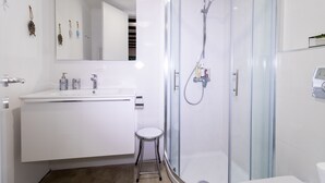 Een moderne badkamer met een douchecabine van glas, een witte wastafel met spiegel en een klein krukje.