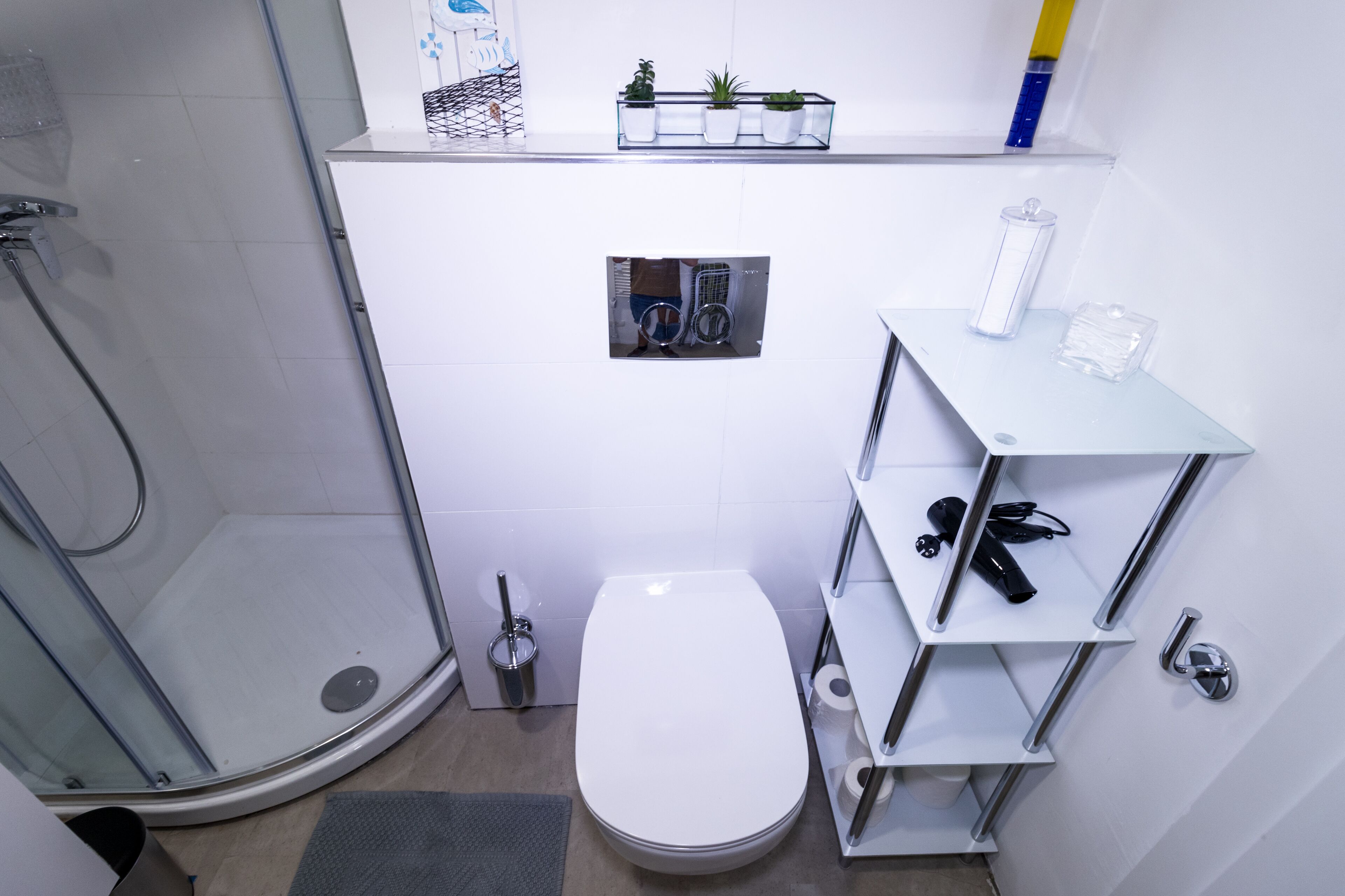 Un baño moderno con cabina de ducha de vidrio, inodoro blanco y estante con artículos de aseo.