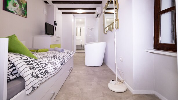 Een slaapkamer met een bed, een televisie, een spiegel en een raam.