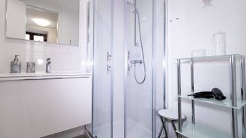A modern bathroom with a glass-enclosed shower, a white sink, and a glass shelf with toiletries.