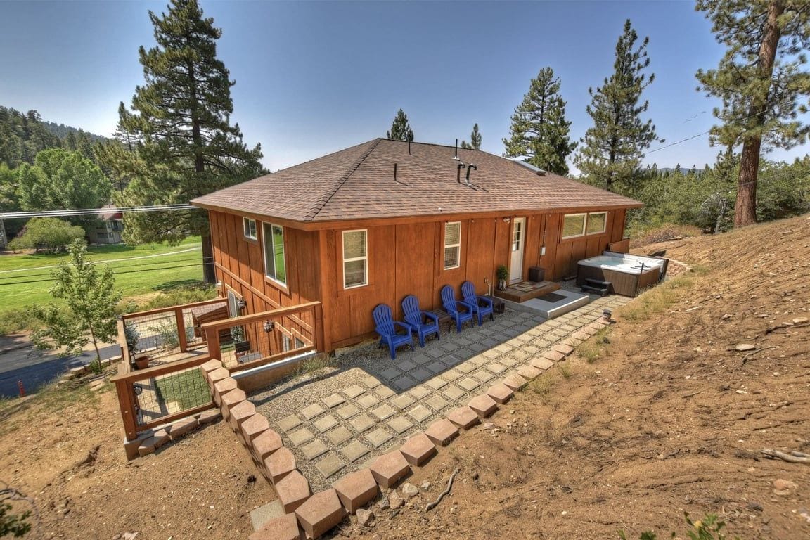 Una cabaña de madera con un patio, mobiliario exterior y vistas a un área boscosa.