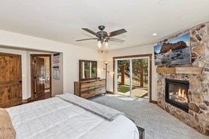 Ein Schlafzimmer mit Bett, Schminktisch, Deckenventilator, Kamin und einem an einer Steinwand montierten Fernseher.