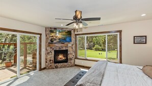 Ein Schlafzimmer mit Kamin aus Stein, Deckenventilator und großen Fenstern mit Blick auf einen Golfplatz.