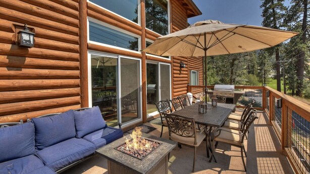 Eine Holzhütte mit einer Terrasse, auf der sich ein Feuerkorb, Gartenmöbel und ein großer Sonnenschirm befinden.