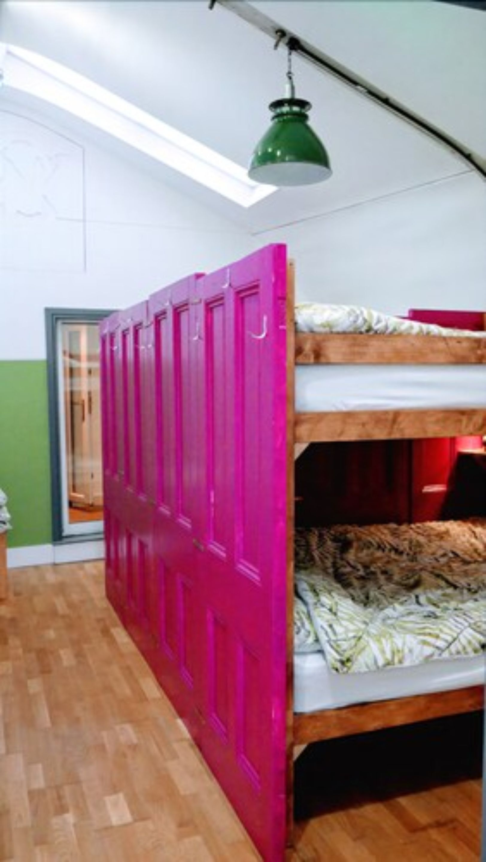 A room with a bunk bed, a bright pink door, and a skylight.