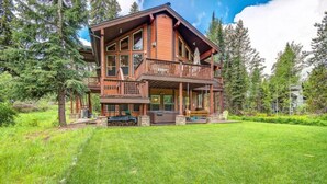 A two-story log cabin with a balcony, surrounded by a well-maintained lawn and tall trees. - McCall Cabin in Spring Mountain Ranch- Shared Pool (McCall)