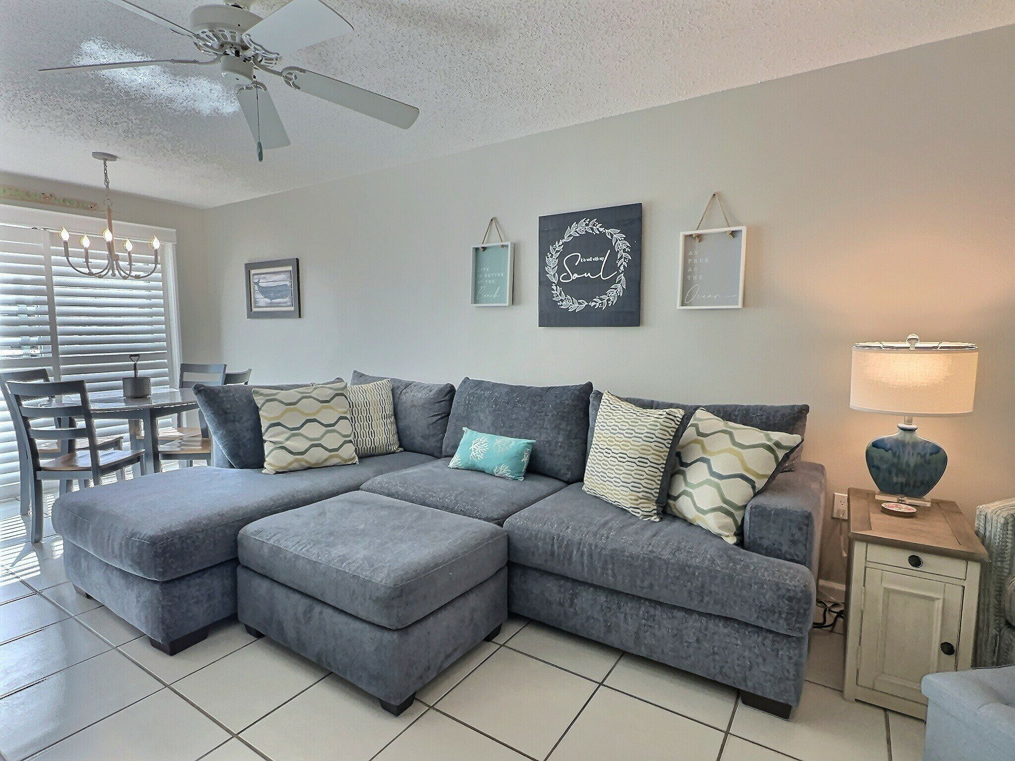 A living room with a grey sectional sofa, a dining table with chairs, a ceiling fan, and wall art.