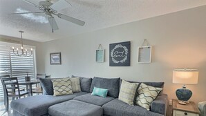 A living room with a grey sectional sofa, a dining table with chairs, a ceiling fan, and wall art. - Enjoy the Siesta Key Beach Life to the fullest! Beach AND Pool Access (Siesta Key)