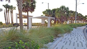 A paved walkway alongside a grassy area with palm trees and a white structure with benches. - Enjoy the Siesta Key Beach Life to the fullest! Beach AND Pool Access (Siesta Key)