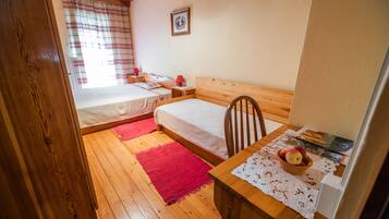 A cozy bedroom with two beds, a wooden table with a bowl of fruit, and a red rug on the floor.