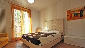 A bedroom with a large bed, a chair, a radiator, and a painting on the wall. - Apartment Alloro - 2 bedrooms, pool, A/C, wifi, pets, see, Marche (Candelara di Pesaro)