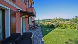 A patio with wicker furniture and a table, a stone pathway leading to a grassy area, and a view of rolling hills in the distance. - Apartment Alloro - 2 bedrooms, pool, A/C, wifi, pets, see, Marche (Candelara di Pesaro)
