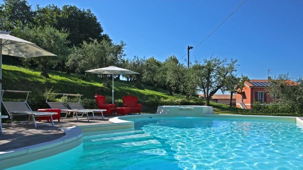 A swimming pool with lounge chairs and umbrellas, surrounded by greenery and a building in the background. - Apartment Alloro - 2 bedrooms, pool, A/C, wifi, pets, see, Marche (Candelara di Pesaro)