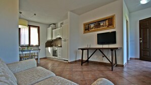 A living room with a sofa, a TV on a stand, a kitchen in the background, and a door to the right. - Apartment Alloro - 2 bedrooms, pool, A/C, wifi, pets, see, Marche (Candelara di Pesaro)