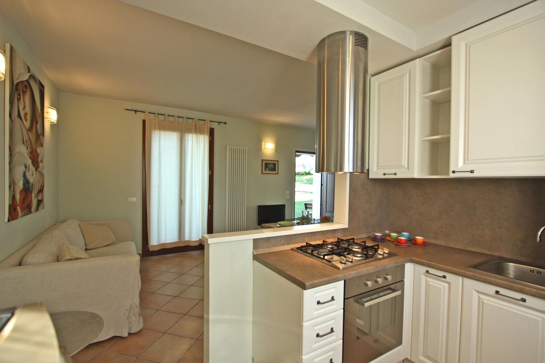 A compact kitchen with white cabinets, a stainless steel range hood, a gas stove, and a built-in oven.