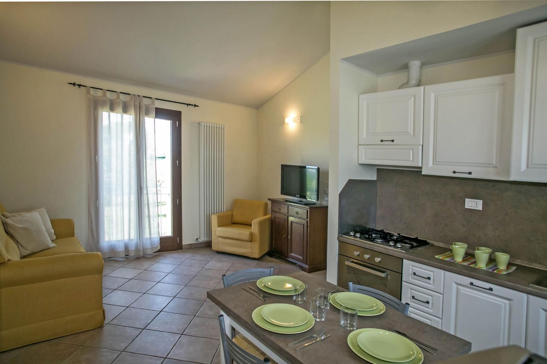 Un espacio habitable compacto con kitchenette, un sofá, una mesa de comedor con platos verdes y un televisor sobre un mueble.