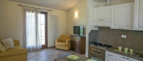 Un espacio habitable compacto con kitchenette, un sofá, una mesa de comedor con platos verdes y un televisor sobre un mueble.