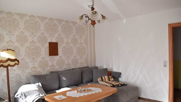 A living room with a grey sofa, a wooden coffee table, a patterned wallpaper, a chandelier, and a lamp. - Nice apartment in the middle of the city and yet in the green (Görlitz)