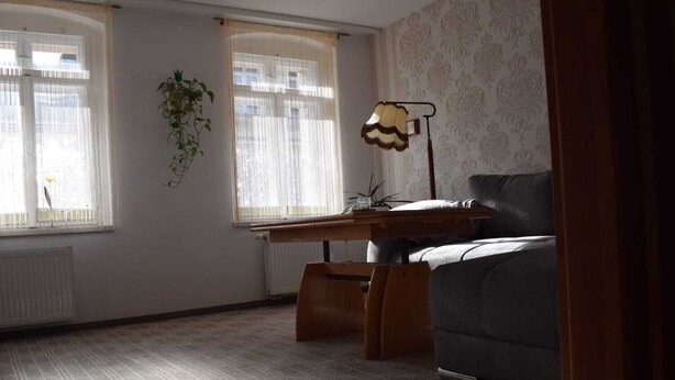 A room with a wooden desk, a grey sofa, and a radiator.