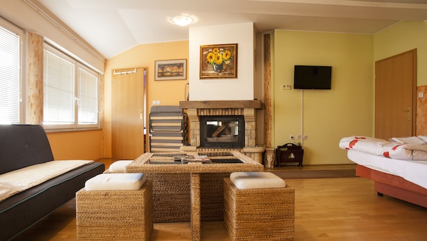 A cozy room with a sofa, a wicker table with cushions, a fireplace, and a television on the wall.