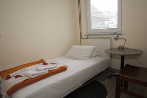 A small, single-bed room with a window, a radiator, and a small table.