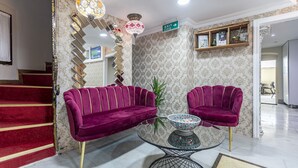 A lobby with a red carpeted staircase, two purple velvet sofas, a glass coffee table with a patterned bowl, and a chandelier. - OttomanZade (Istanbul)