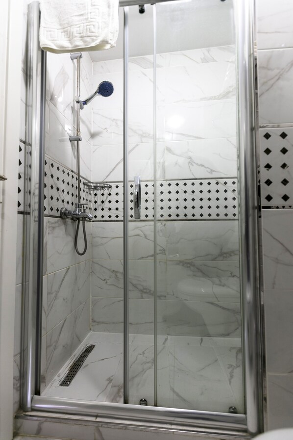 A glass-enclosed shower with a handheld showerhead and a wall-mounted faucet. - OttomanZade (Istanbul)