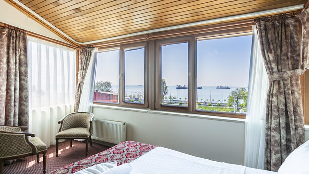 A hotel room with a large window, a bed, a chair, and a radiator. - OttomanZade (Istanbul)