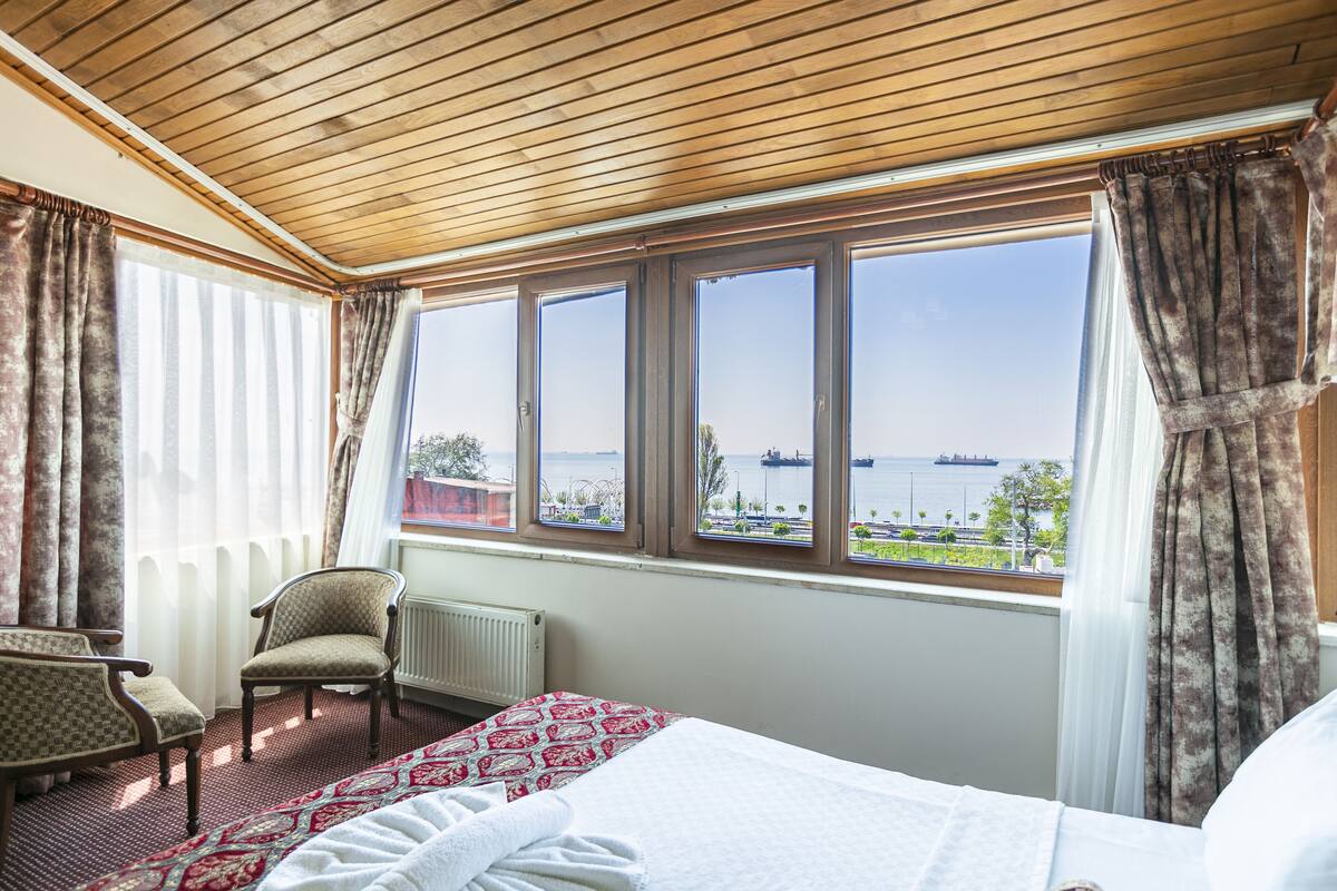 A hotel room with a large window, a bed, a chair, and a radiator.