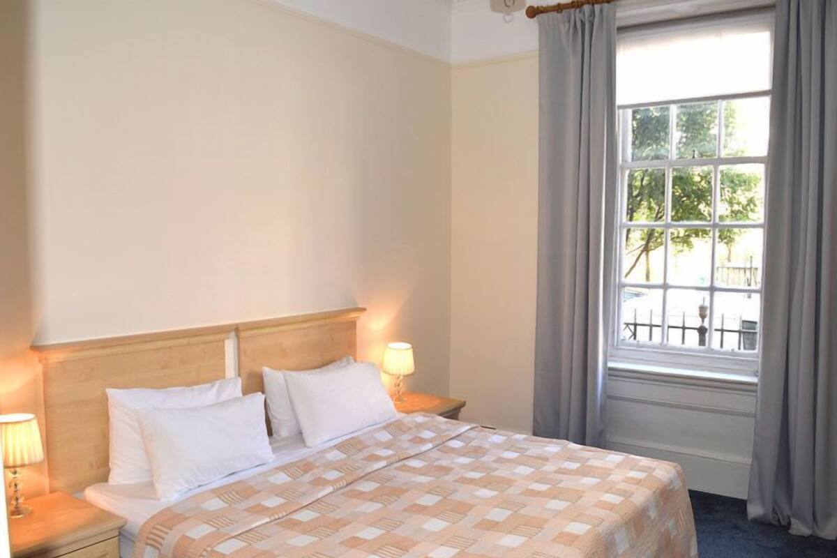 A hotel room with a bed, two bedside lamps, a window with curtains, and a view of the outdoors.