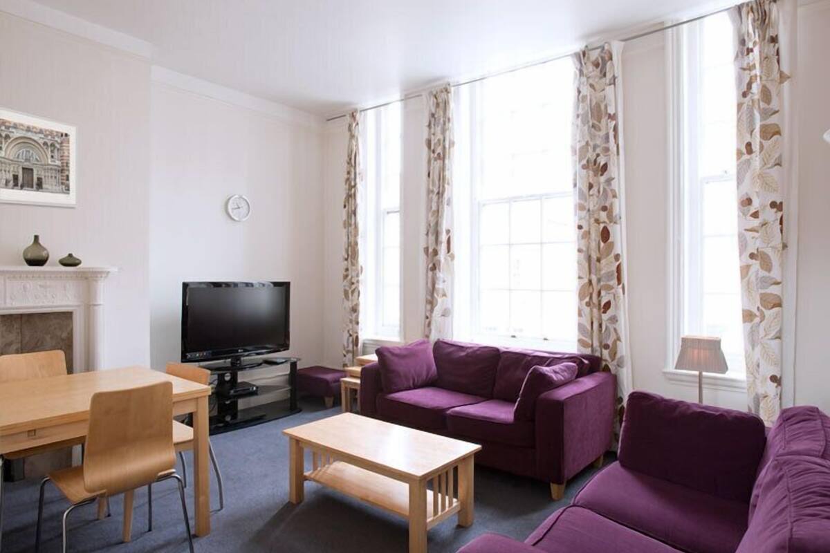 A living room with a fireplace, a television, a dining table with chairs, and a purple sofa.