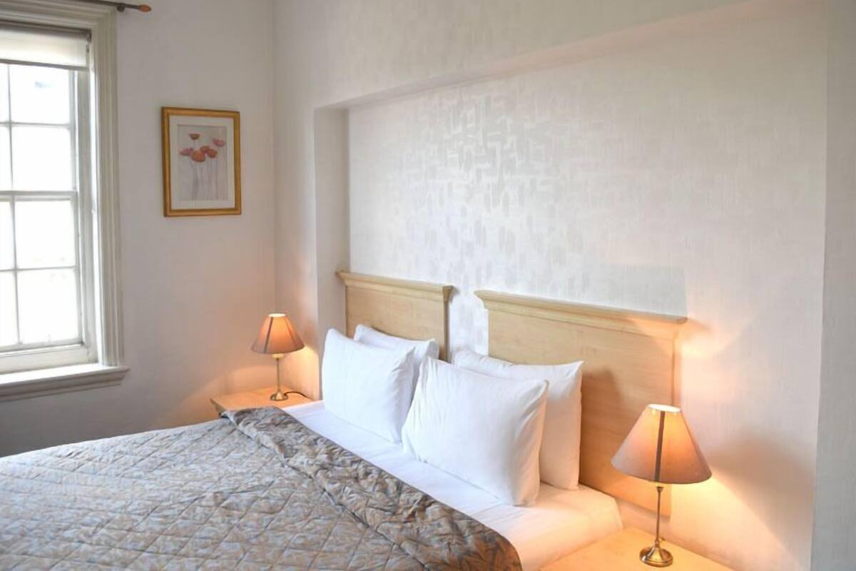 A neatly made bed with a quilt, two bedside lamps, and a framed picture on the wall.