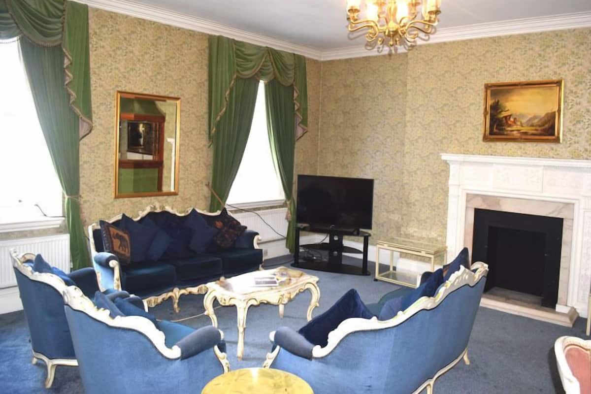 A living room with a sofa set, television, fireplace, and green curtains.