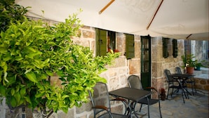 Eine Terrasse im Freien mit Steinmauern, grünen Fensterläden und einem Tisch mit Stühlen.