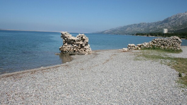 Ein Kiesstrand mit Felsformationen und einem Berg im Hintergrund.