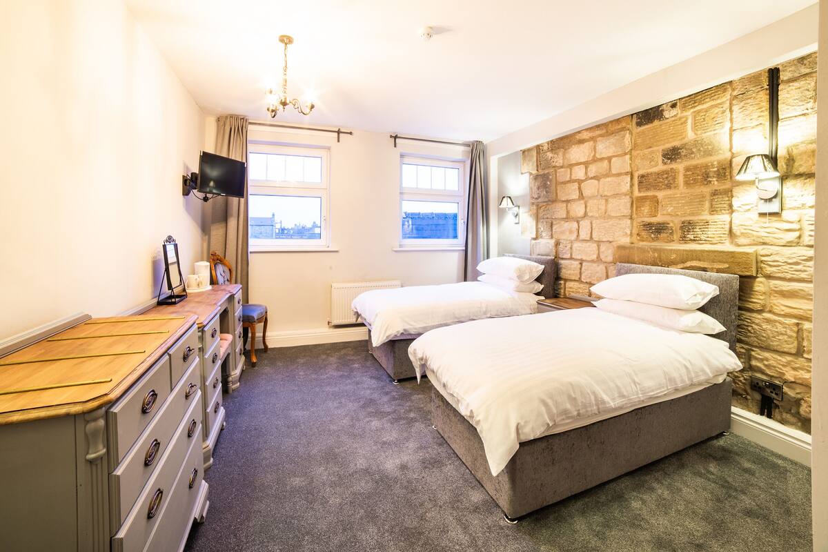 A bedroom with two beds, a dresser, a TV, and a stone accent wall.