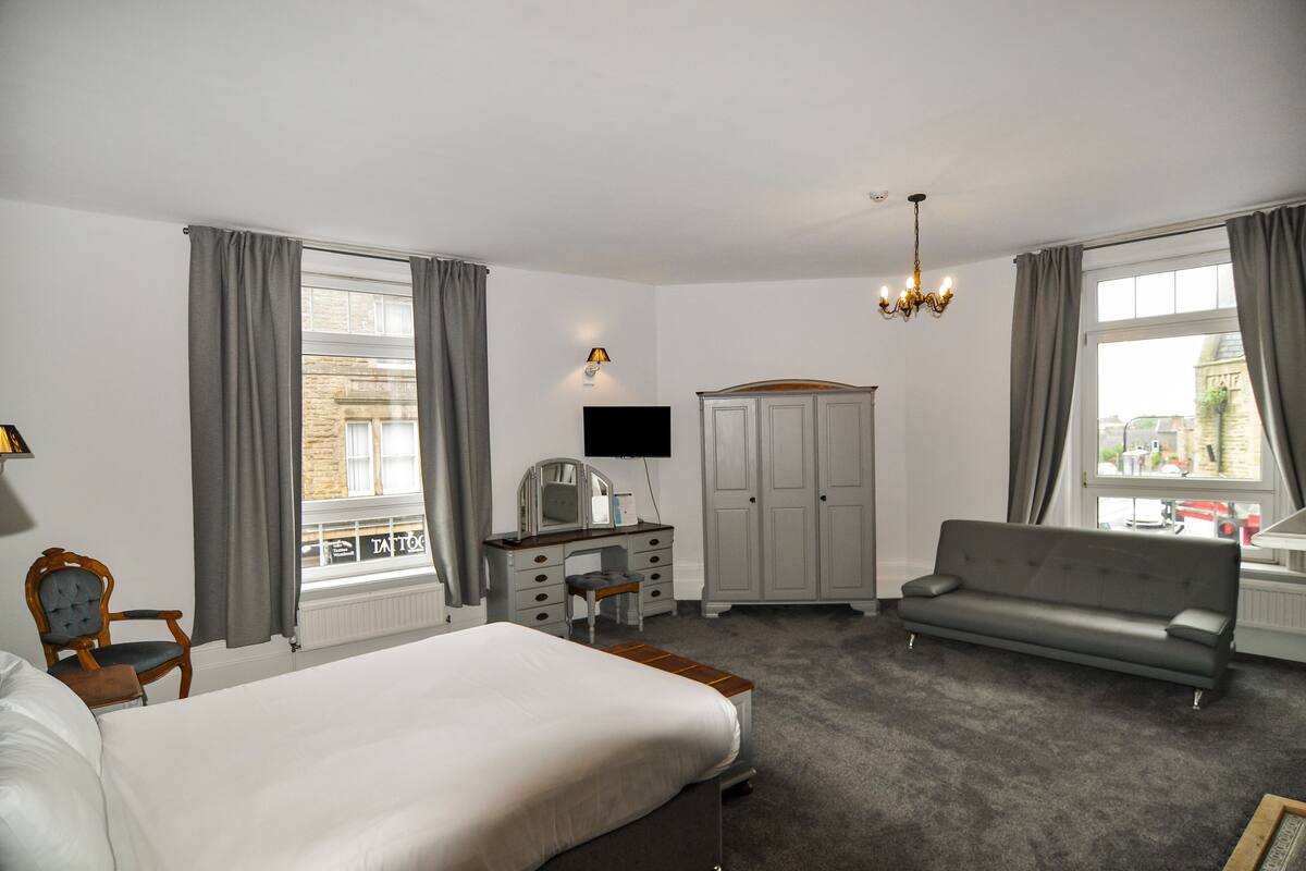 A hotel room with a bed, a desk with a chair, a sofa, a wardrobe, and a TV.