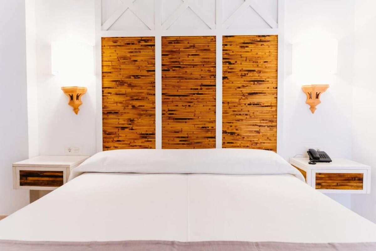 A bedroom with a large bed, wooden headboard, white walls, and bedside tables with lamps.