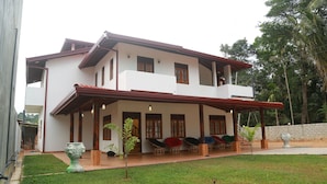 A two-story house with a covered porch, outdoor seating, and a small lawn.