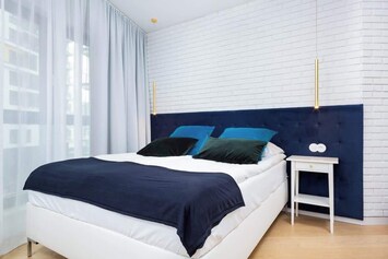 A modern bedroom with navy and white bedding on a double bed, complemented by light wooden furniture and a bright atmosphere.