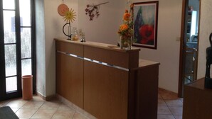 A reception area with a wooden counter, a vase with flowers, a painting, and a sun decoration on the wall. - Pension Anna Gastronomie (Loebau)