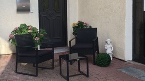 A brick-paved patio with two black wicker chairs and a small table, a dark door, and a wall-mounted light fixture. - Pension Anna Gastronomie (Loebau)