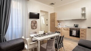 A modern living room with a dining table, chairs, and a sofa. A kitchen with a stove and cabinets is visible in the background. - I Fiumi Di Navona (Rome)
