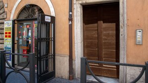 A building with a large brown door and a glass-fronted phone booth with various signs. - I Fiumi Di Navona (Rome)