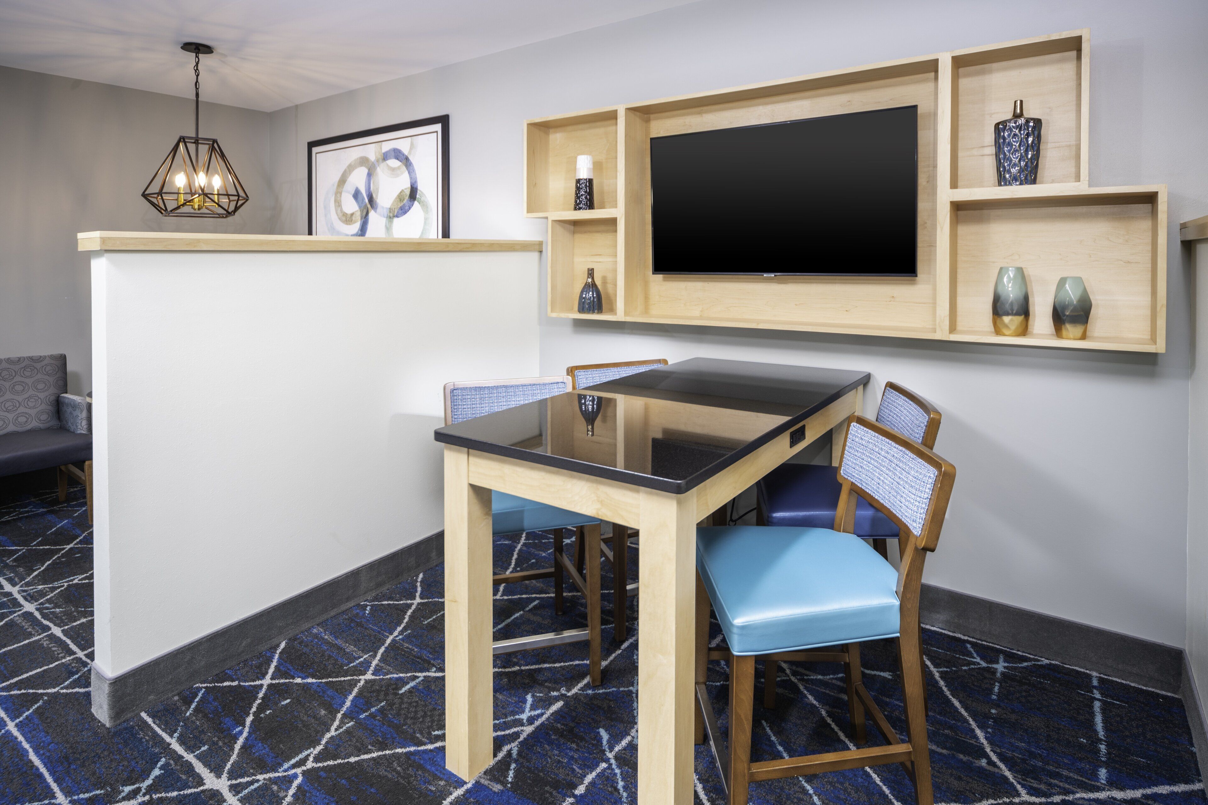 A modern room with a dining table, chairs, a TV mounted on the wall, and a patterned carpet.