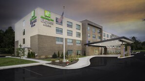 Un hotel Holiday Inn Express con fachada de ladrillo, un asta con la bandera estadounidense y una zona de estacionamiento techada.