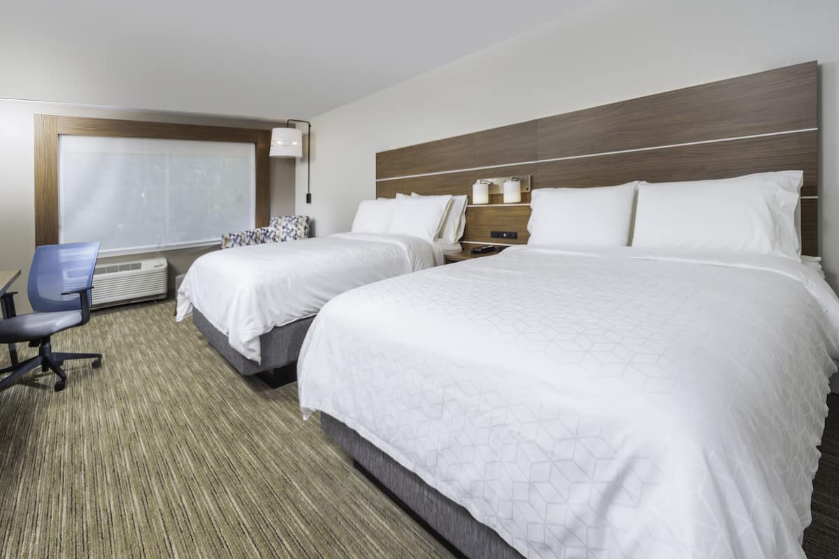 A hotel room with two beds, a desk, and a chair.